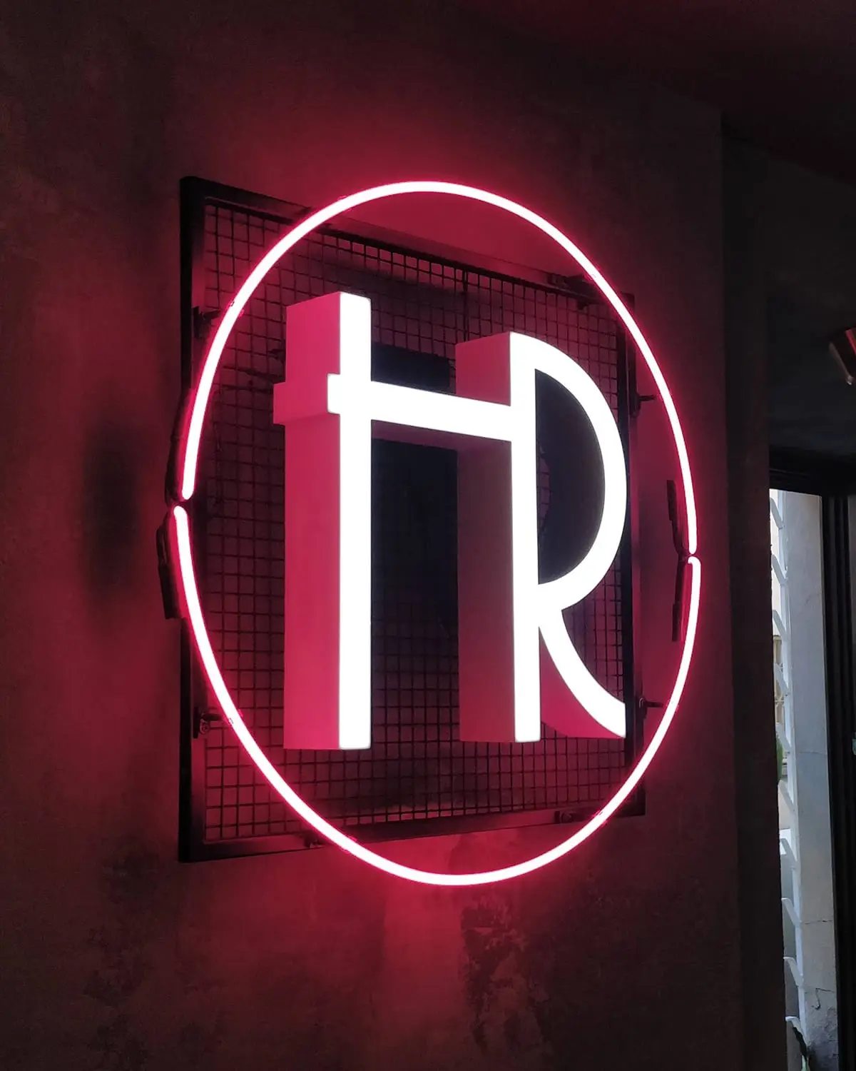 Hollywood Room logotipas su rožiniu neono žiedu ant tinklo rėmo