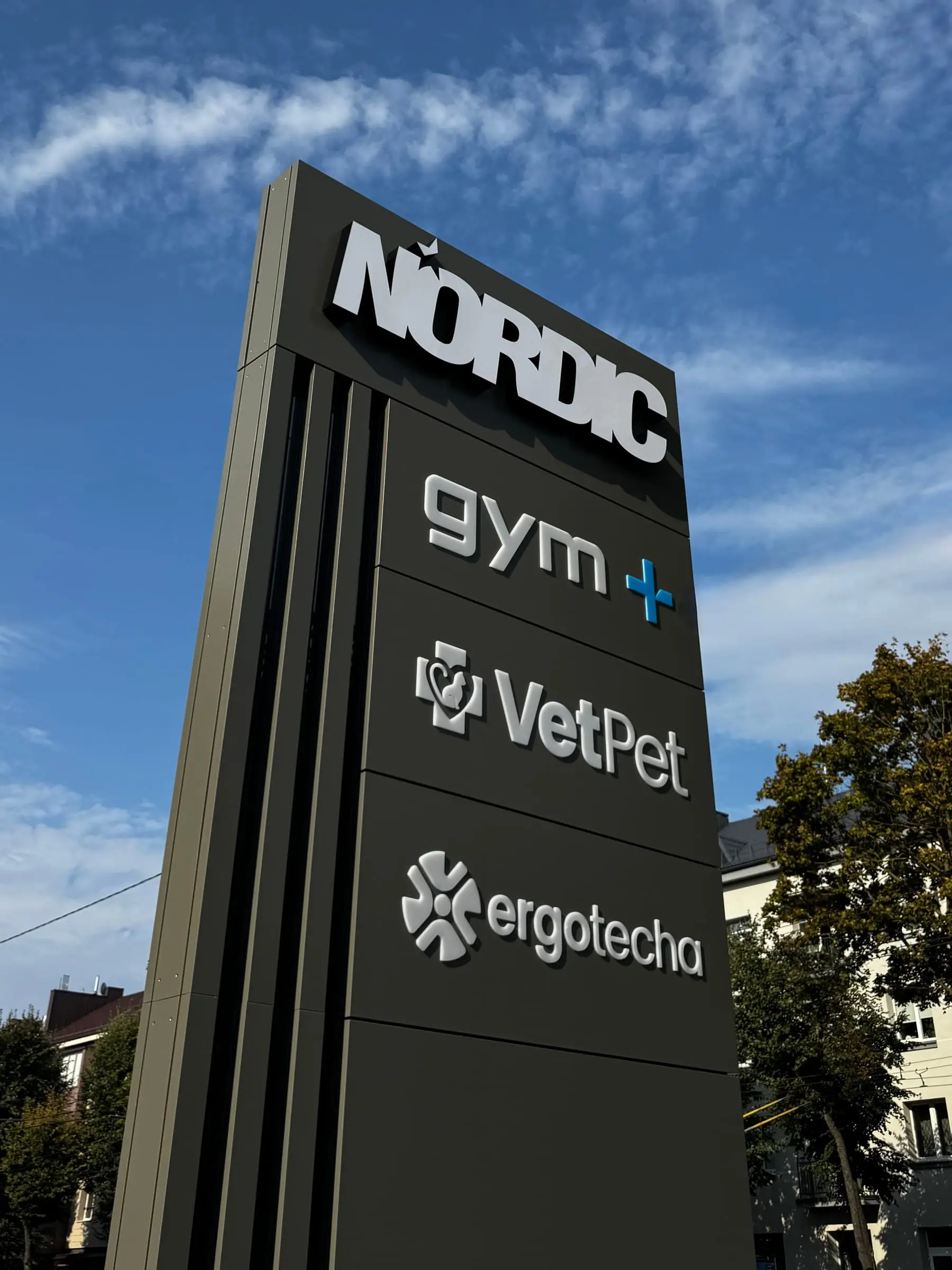 NORDIC pilonas su gym+, VetPet ir ergotecha logotipais dienos šviesoje