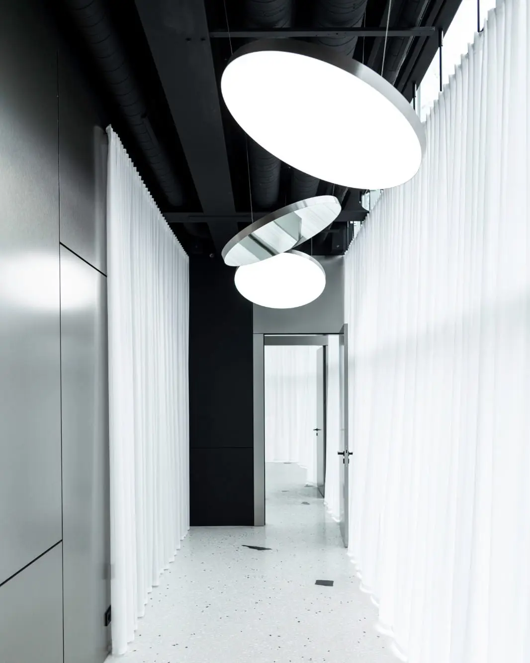 Sculpta koridorius su apvaliomis LED panelėmis ir baltomis užuolaidomis